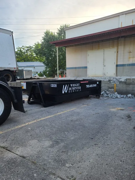 A black yard dumpster parked on an asphalt surface