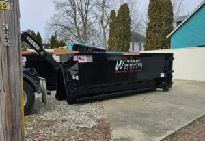 A black wright dumpster rental container attached to a truck, parked on a concrete surface in a residential area