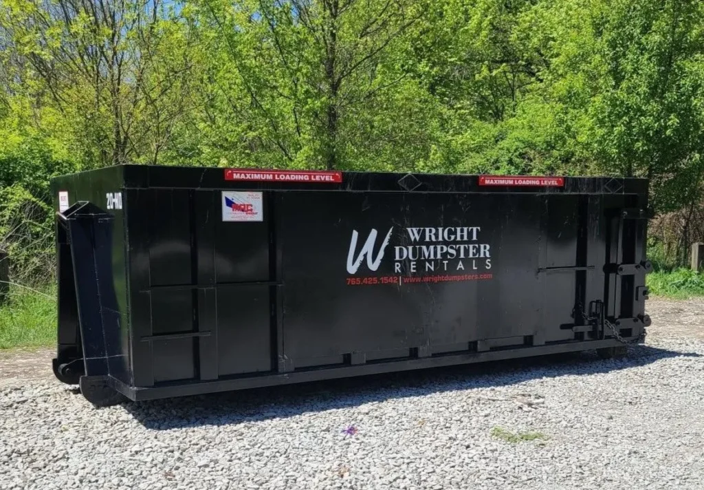 A black-colored yard dumpster with trees in the background